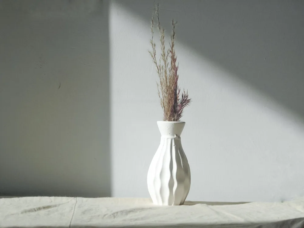 A dried plant in a white vase by a window