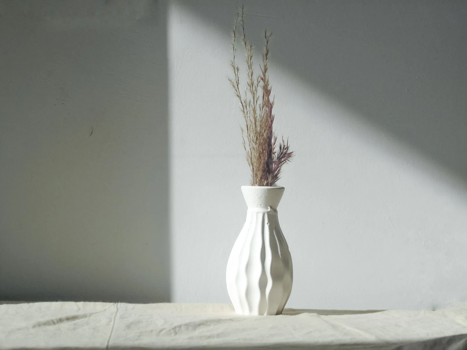 A dried plant in a white vase by a window